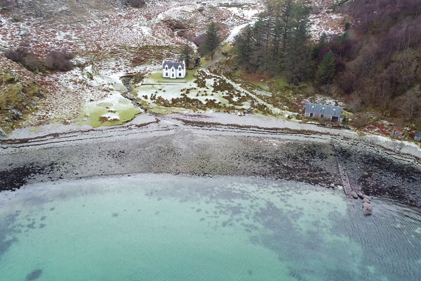 Aerial view of a white cottage above a turquoise bay, with the garden, shore line, track and distances marked